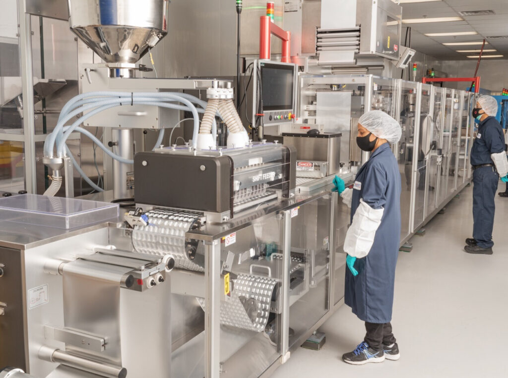 Technician operating a blister packaging machine in a cleanroom environment.