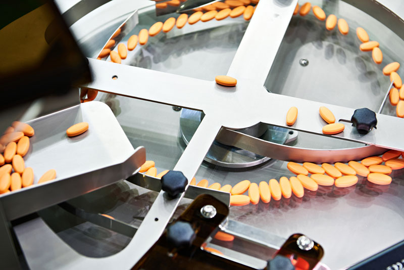 Close-up of orange tablets being sorted by a supplement manufactuirng facility.