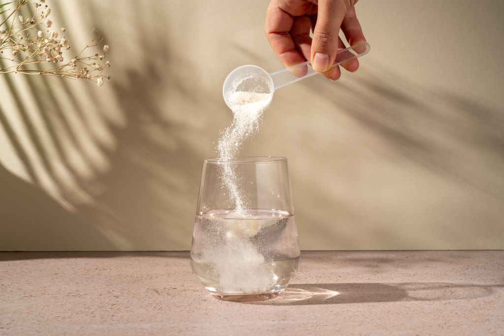 A scoop of a collagen supplement being added to a glass of water.