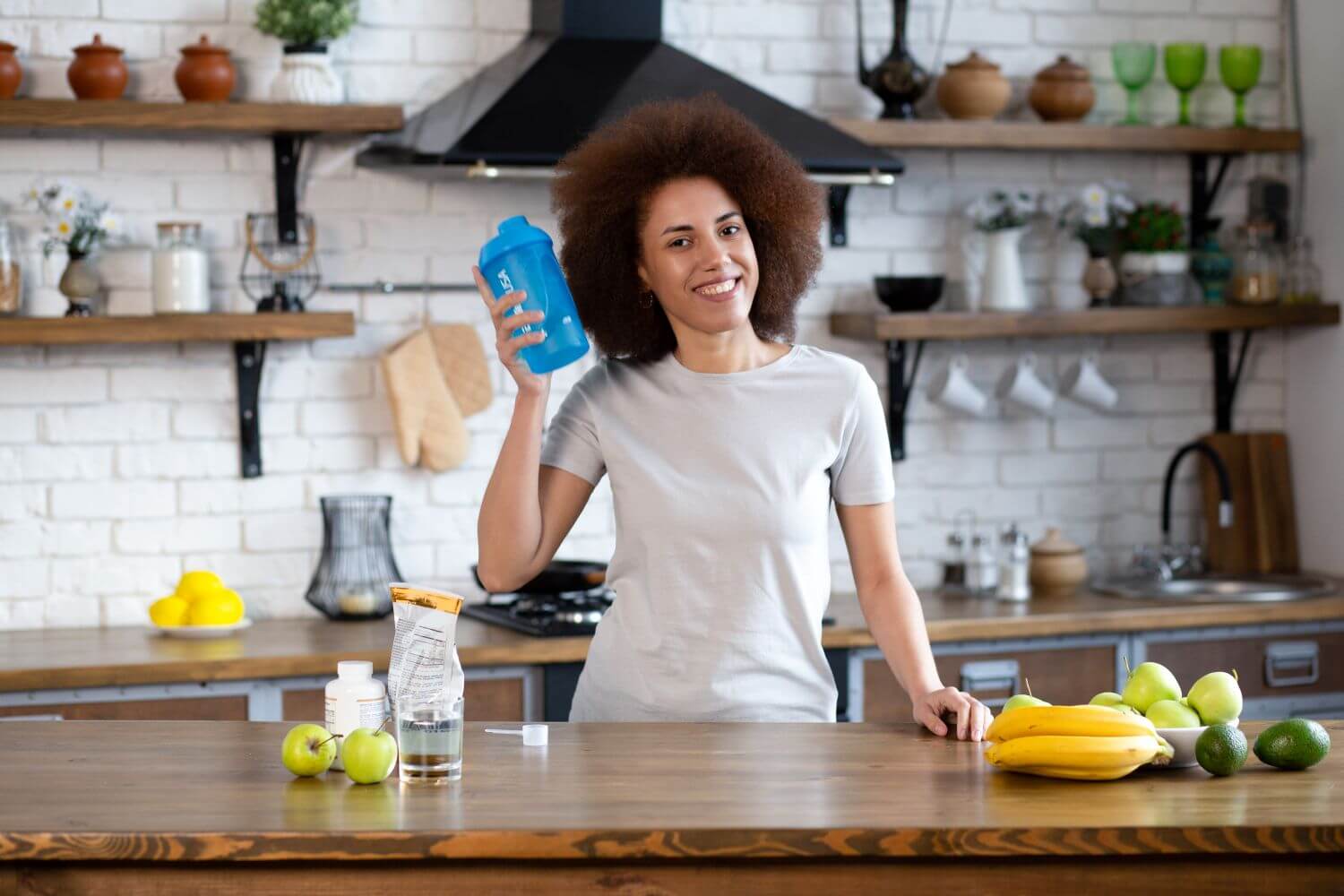 Woman holding a supplement shaker in a kitchen with fruit, highlighting supplements for energy focus and mood