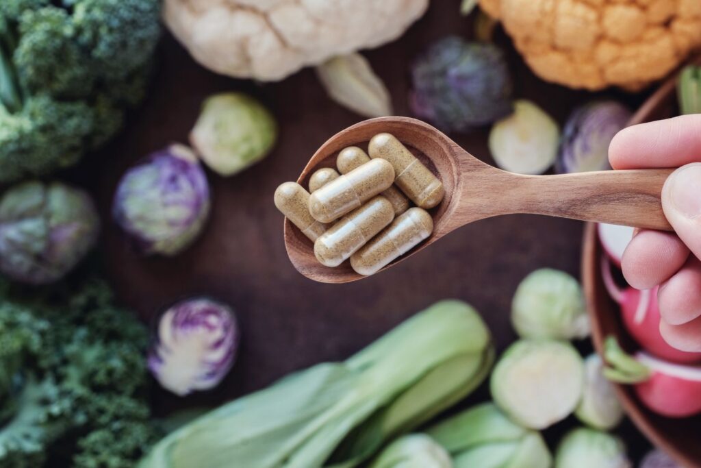 What are nutraceuticals? Dietary supplement capsules on a wooden spoon surrounded by fresh vegetables.