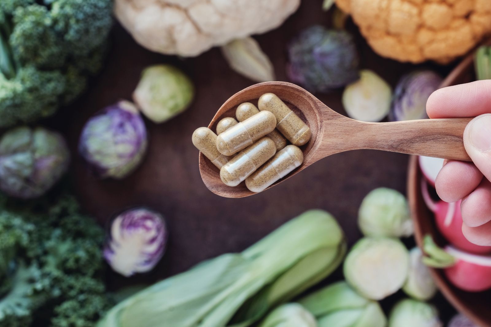 What are nutraceuticals? Dietary supplement capsules on a wooden spoon surrounded by fresh vegetables.